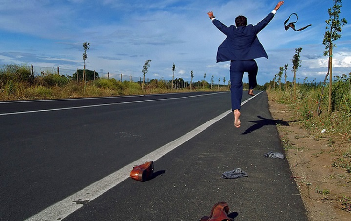 Un uomo in giacca e cravatta scappa a gambe levate su una strada deserta